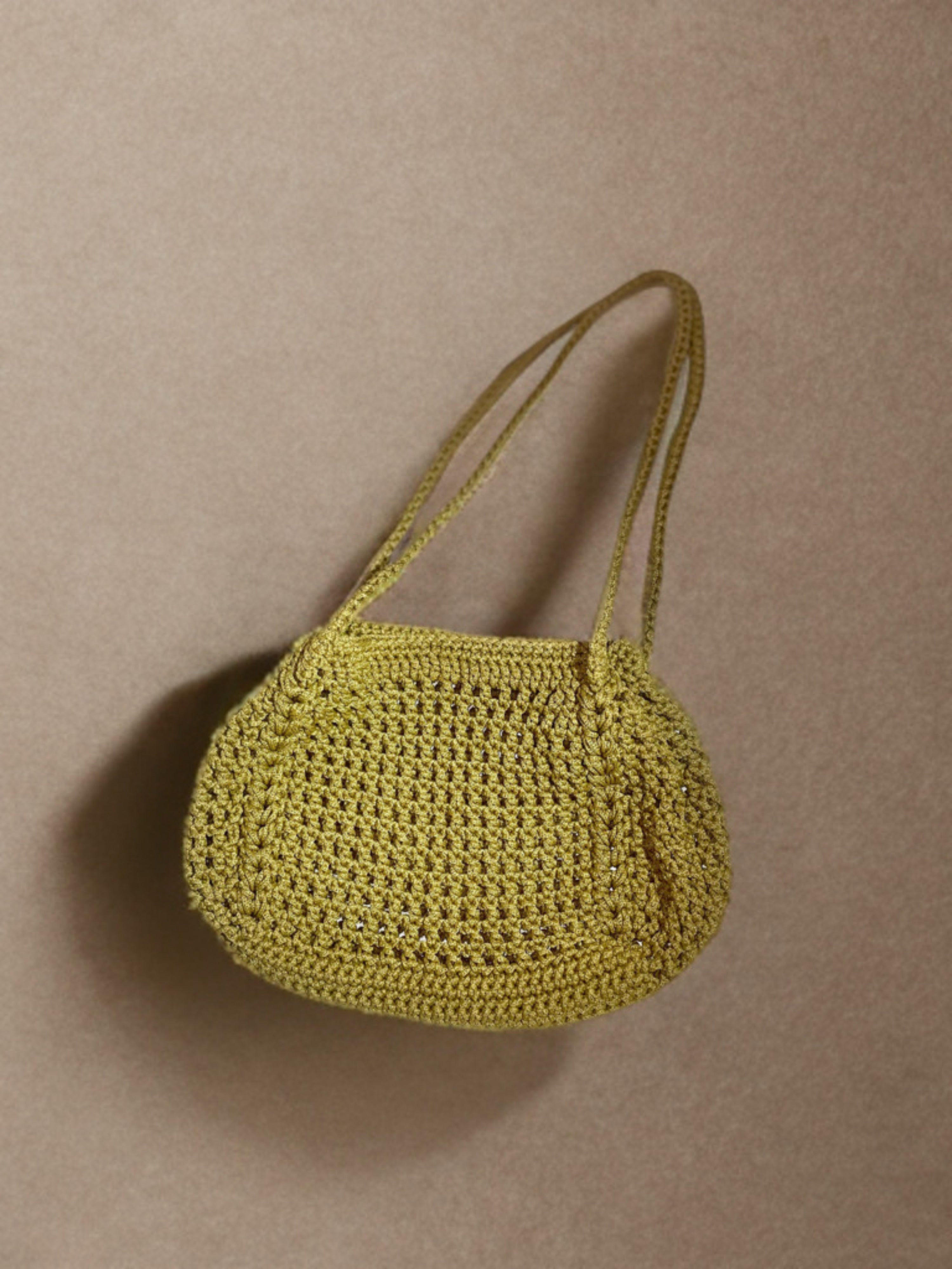 A small yellow crocheted shoulder bag with a single strap, photographed against a plain beige background.